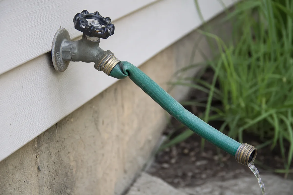 A garden hose kinked at the spigot restricting flow