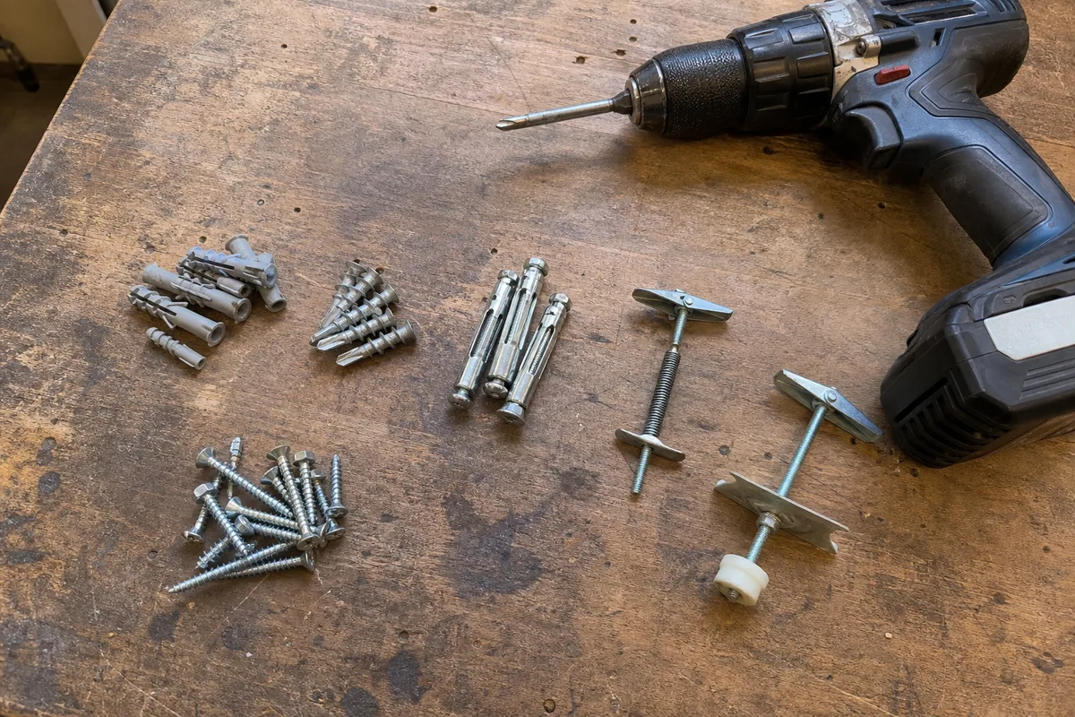 An assortment of wall anchors, screws, and a drill laid out on a workbench