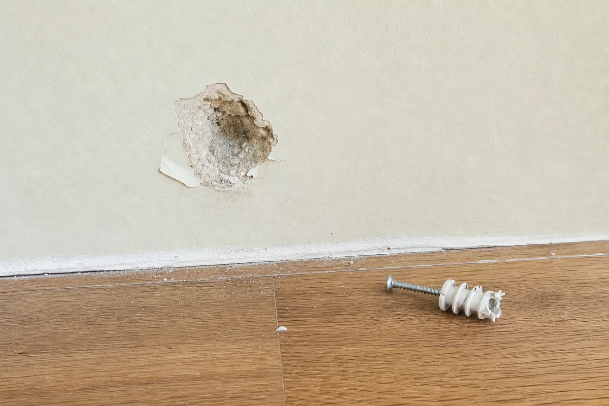 A failed plastic anchor pulled out of drywall leaving a cone-shaped hole