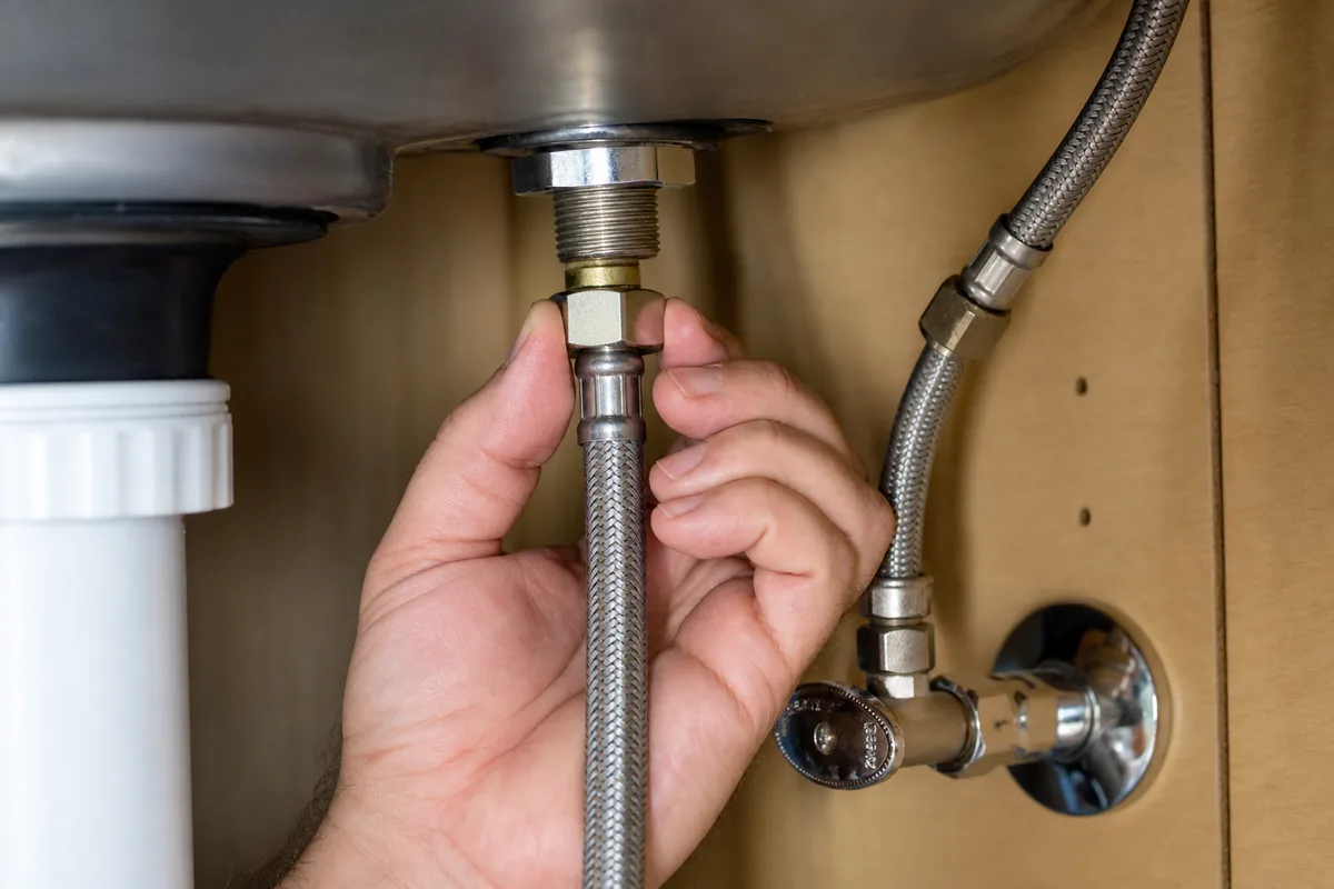 Hand tightening a braided water supply line by hand under a sink