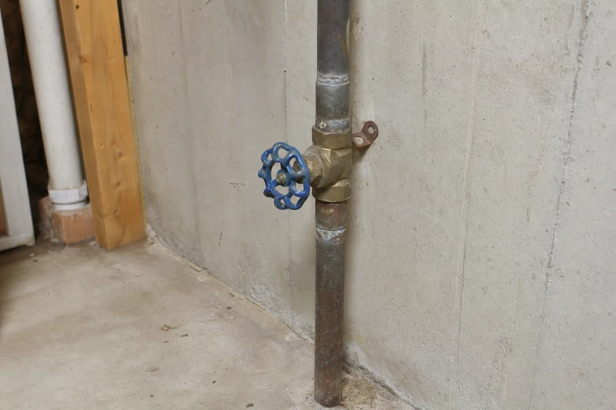 A main water shutoff valve on a pipe near a basement wall